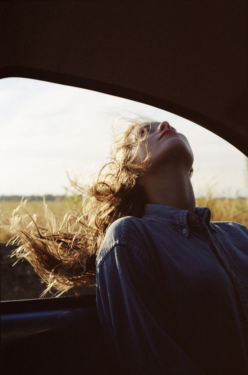 Mujer en un coche con el pelo largo sacando la cabeza por la ventana