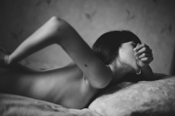 Mujer tumbada en la cama mordiéndose la muñeca.
