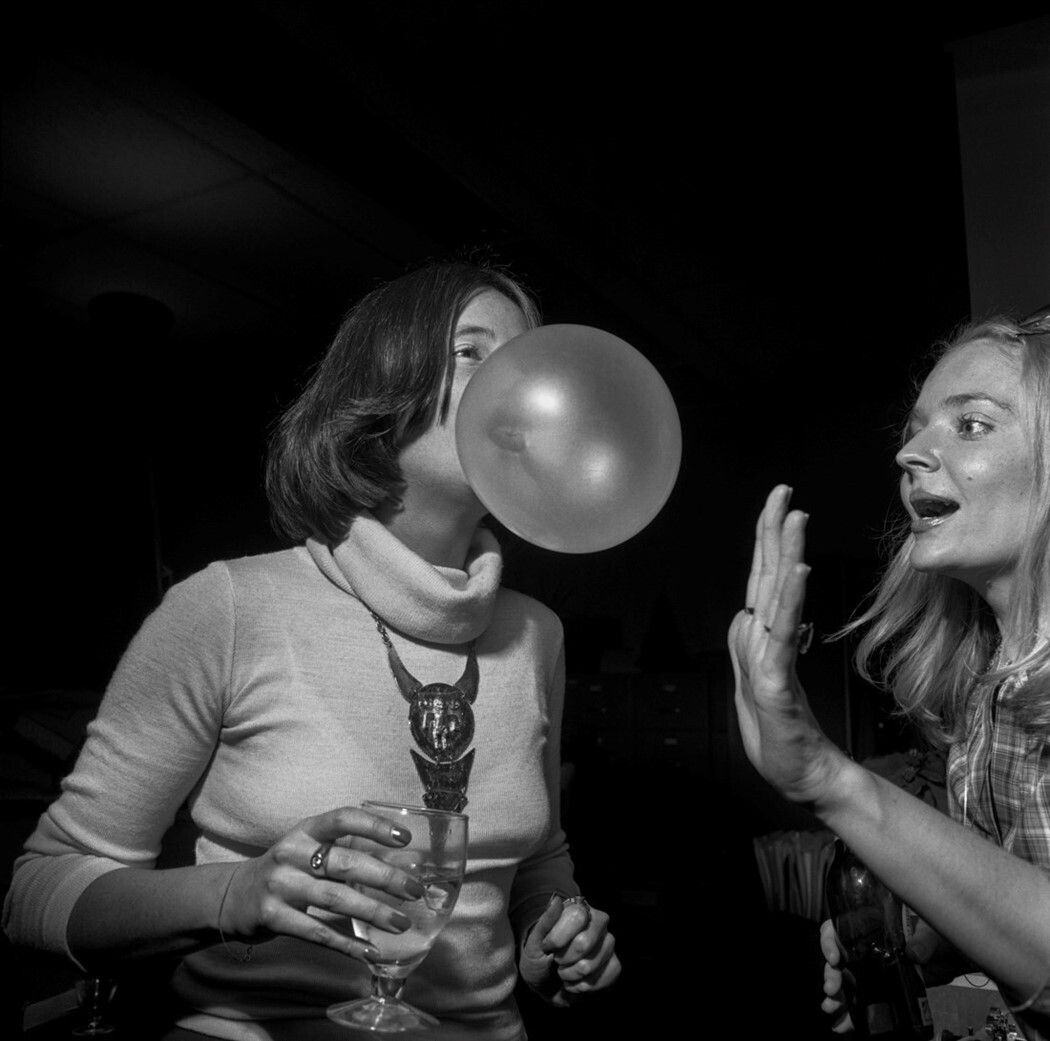 una chica intenta explotar una pompa de chicle a otra chica en una fiesta de la New York Magazine