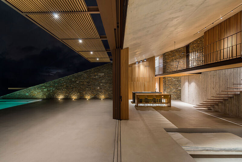 interior de una vivienda forrada en madera y piedra y con una piscina iluminada para la noche