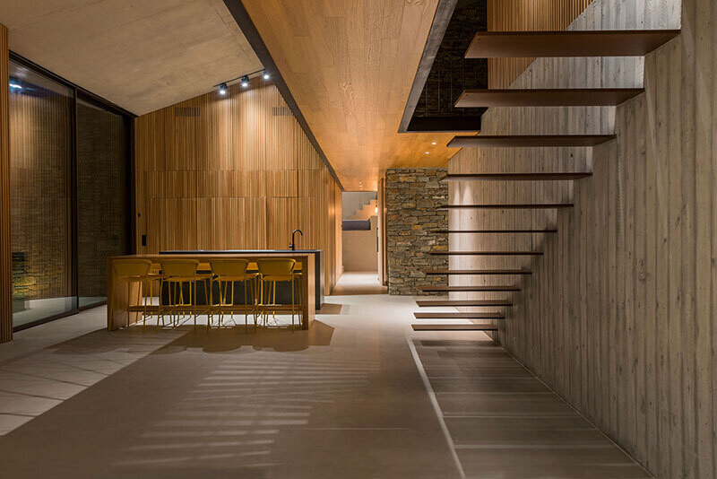 interior de una vivienda forrada en madera y piedra y con una piscina iluminada para la noche