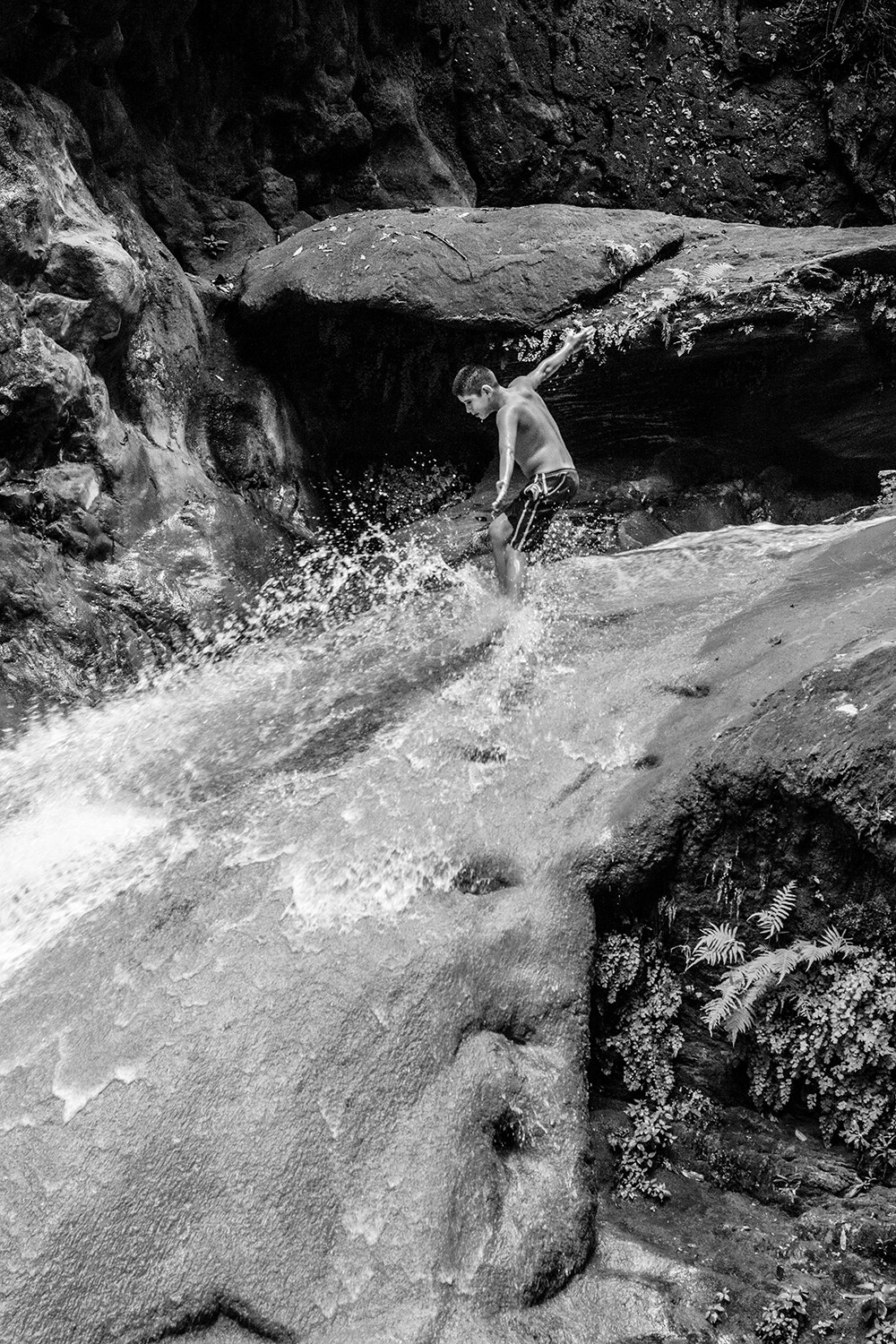 Foto en blanco y nego de un niño jugando en una cascada de agua