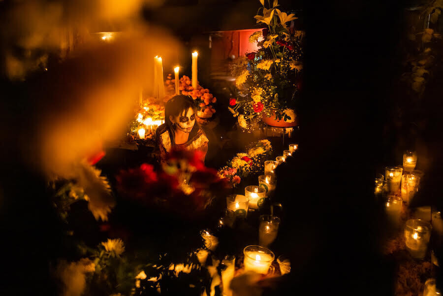 una chica con la cara pintada rezando y encendiendo velas en el Día de Muertos en México