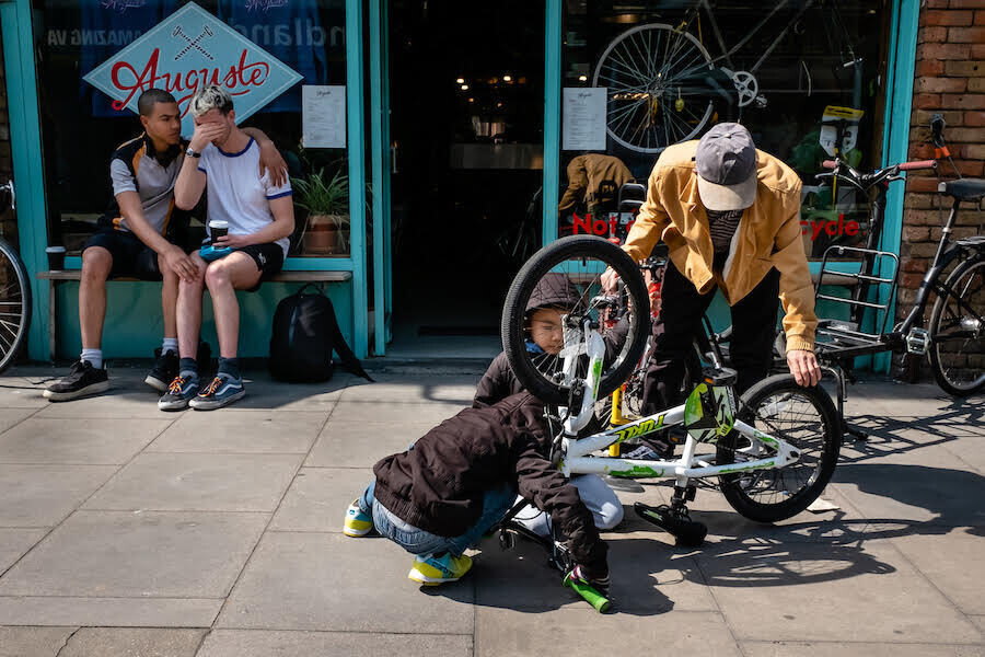 unos niños arreglan una bici y en el fondo un amigo consuela a otro que está llorando