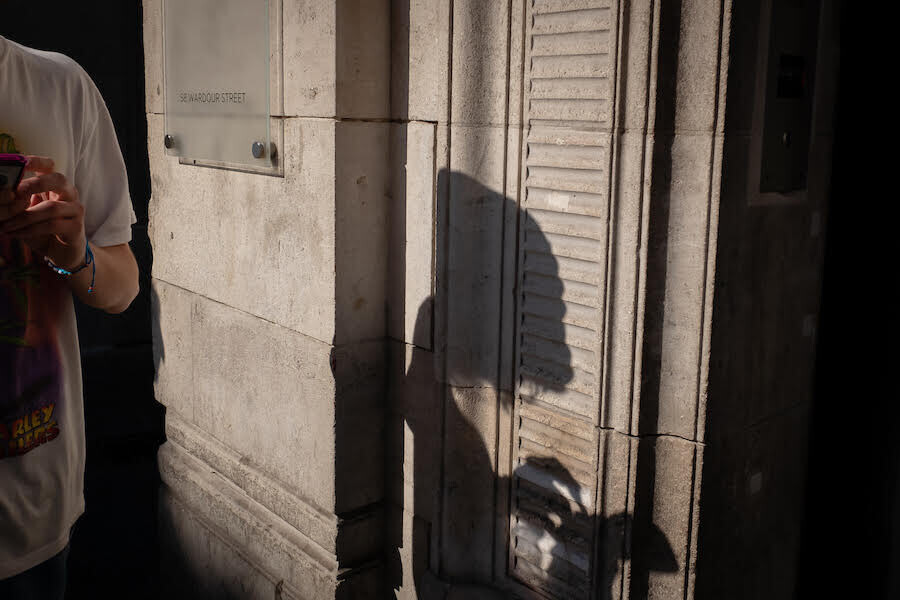 un chico mira el móvil por la calle y la sombra que proyecta es la de un alienígena