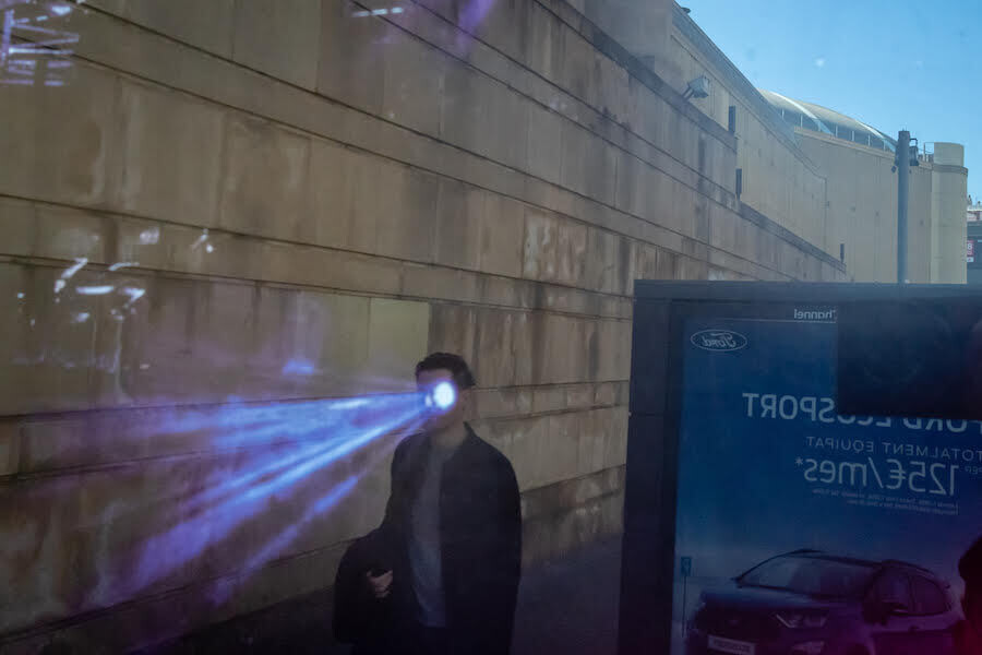 un hombre por la calle proyecta una haz de luz por su ojo en un extraño efecto óptico