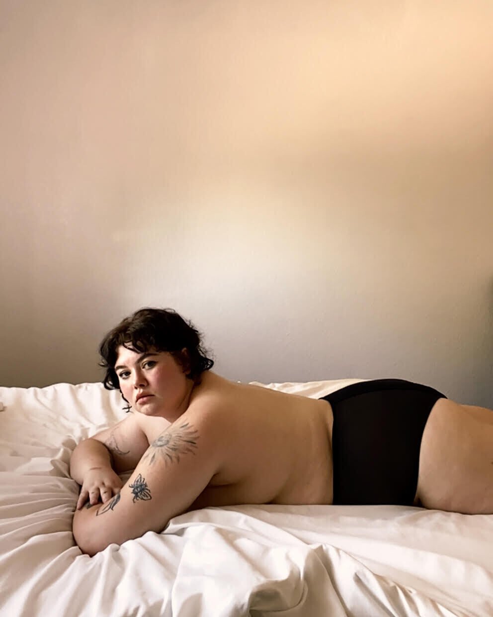 Fotografía de una mujer con el torso desnudo tumbada sobre su cama