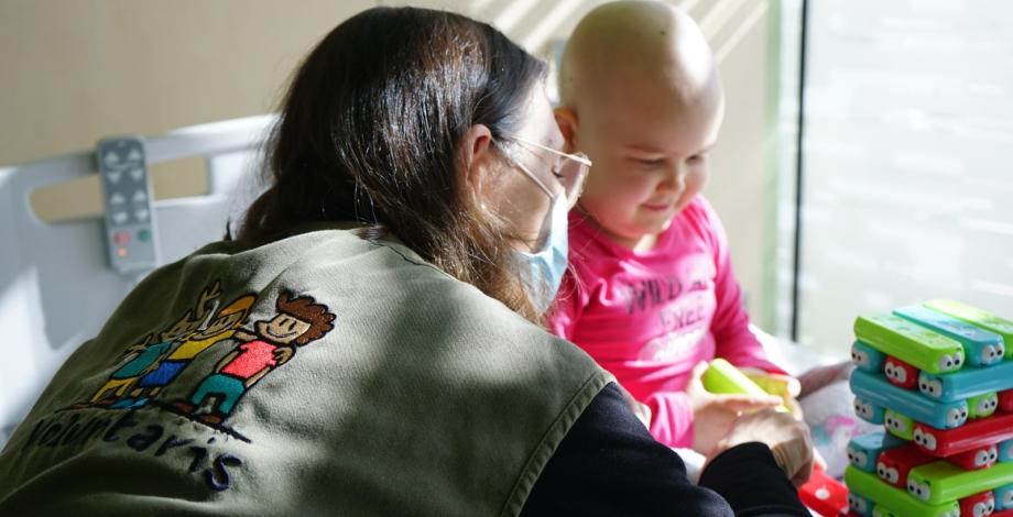 Voluntario ayudando a un niño con cáncer en un hospital.