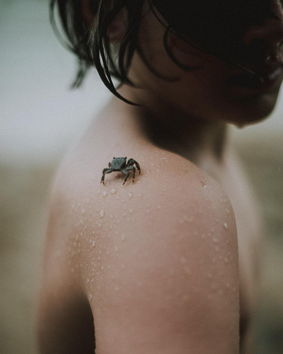 Un niño mojado de la playa con un pequeño cangrejo en el hombro.